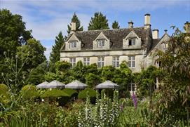 The gardens of The Pig - in the Cotswolds with parasols and seating in front of the wisteria covered house