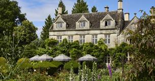 The gardens of The Pig - in the Cotswolds with parasols and seating in front of the wisteria covered house