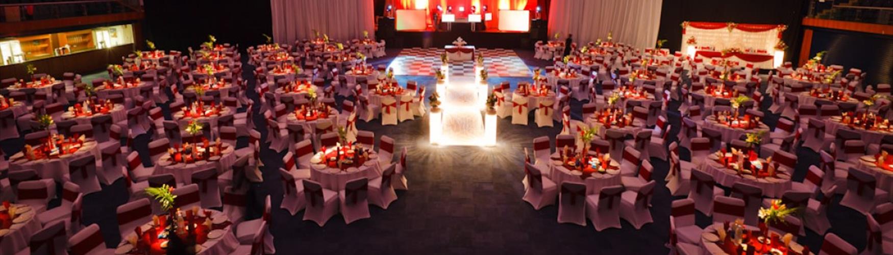 Gala dinner at The Centaur, Cheltenham Racecourse. A stage is set for a band to play behind a chequered dancefloor and round table decorated with flowers