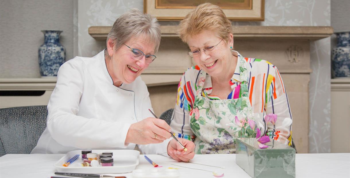two people painting on a sugar flower at a table