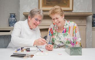 two people painting on a sugar flower at a table