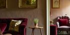 A red velvet sofa in a seating area with antique pictures on the wall