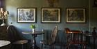 Tables for dining in front of a muted green wall with historic prints hanging